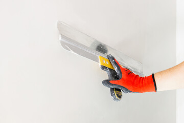 A professional finisher painter levels the walls with putty with a wide spatula - wall decoration...