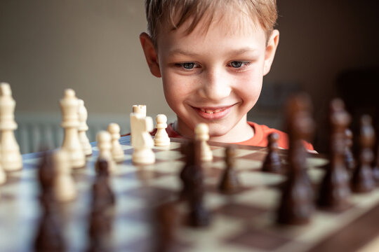 Young white child playing a game of chess on large chess board. Chess board on table in front of school boy thinking of next move