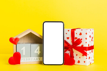 mobile phone with blank screen on colored background with hearts, calendar and gift box, valentine day 14 february concept perspertive view flat lay