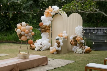  Creative gender neutral baby shower or birthday decoration in the garden. Bohemian style outdoor event set up with balloons. White cream peach caramel balloon arch kit. © triocean
