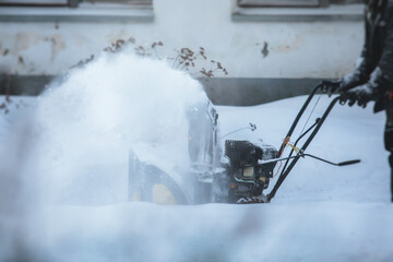 Naklejka na ściany i meble Process of removing snow with portable blower machine, worker dressed in overall workwear with gas snow blower removal on the street during winter
