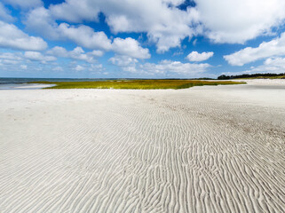 Wide angle view of sandbar with sea grass, dunes, and blue sky and clouds