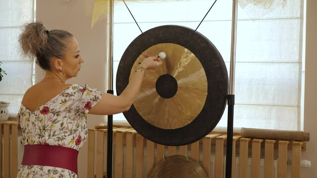Woman makes the sound of a gong with small soft mallet. Gong and little gong hammer