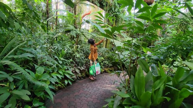 footage of an African American woman with long sisterlocks wearing a brown coat and sunglasses walking in the garden with lush green trees and plants at Atlanta Botanical Garden in Atlanta Georgia USA