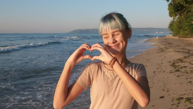 Teen hand heart against sea. A happy teen girl make a heart with her hands against blue sea. A concept of happy joyful summer relaxation.