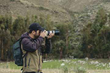 Photographer taking pictures with his camera in a green valley of the Andes mountain range in Peru. Concept professions, people and vacations.