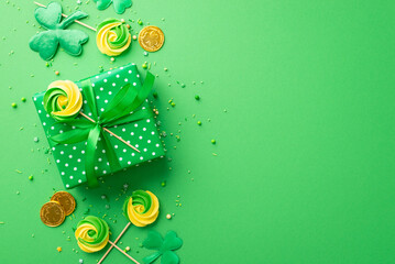 Saint Patrick's Day concept. Top view photo of giftbox with ribbon bow meringue candies gold coins trefoils and sprinkles on isolated green background with empty space