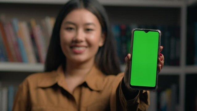 Close-up smiling korean woman businesswoman holding phone showing green screen smartphone touchscreen touch display mockup with chroma key advertise mobile application promote digital device cellphone