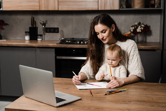 Mom and toddler daughter draw pictures with colored pencils from laptop. Developing drawing lesson for child toddler at home. Maternity leave.