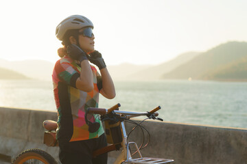 Asian woman cyclist wearing a helmet getting ready for a bike ride around the lake in the morning with beautiful mountain view in the background.