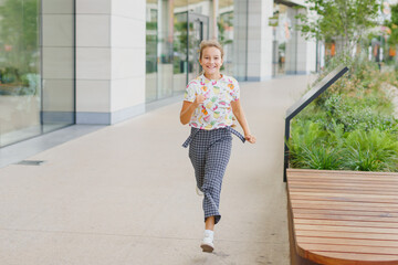 Happy little cute girl with headphones runs towards the city