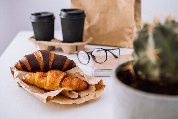 Delicious brown and chocolate croissants with coffee cups, having lunch at workplace, food delivery concept