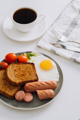 Breakfast plate with cup of black coffee, grilled sausage and whole wheat toast with fried egg and cherry tomatoes on a plate
