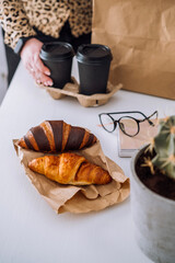 Delicious brown and chocolate croissants and coffee cups, woman having lunch at workplace, food delivery concept