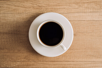 Flat lay black coffee in a white cup with a saucer on a wooden table