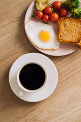 Homemade breakfast with cup of black coffee, fried egg and toast with tomatoes and avocado on a plate