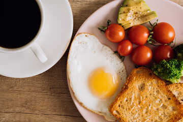 Close up homemade breakfast with cup of black coffee, fried egg and toast with tomatoes and avocado on a plate