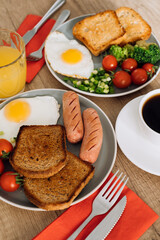 English breakfast with cup of black coffee and orange juice, grilled sausage and whole wheat toast with fried egg and cherry tomatoes on a plate