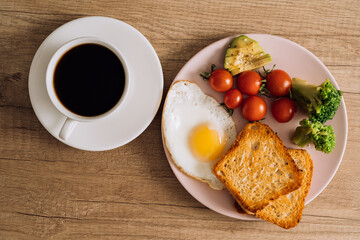 Flat lay homemade breakfast with cup of black coffee, fried egg and toast with tomatoes and avocado on a plate