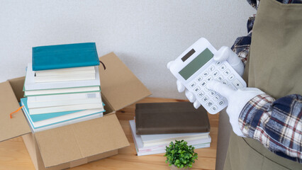 本と電卓とエプロンを着た男性｜断捨離・片付け・古本買取イメージ