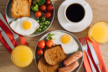 Flat lay English breakfast with cup of black coffee and orange juice, grilled sausage and whole wheat toast with fried egg and cherry tomatoes