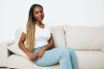 Obraz premium Happy african american woman sitting at home on sofa, rest and vacation smile, light background. Relaxed home lifestyle, day off.