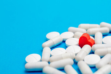 Red pill in the shape of a heart on a background of white pills and a blue background. The concept...