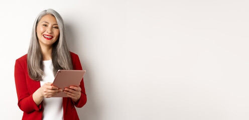 Business. Successful senior businesswoman working with digital tablet and smiling, standing in red...