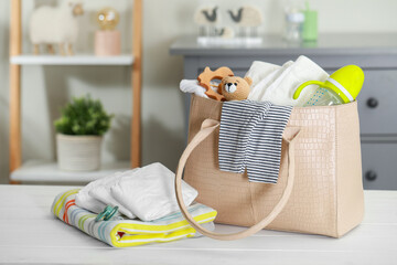 Mother's bag with baby's stuff on white wooden table indoors