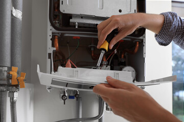 Man repairing gas boiler with screwdriver indoors, closeup