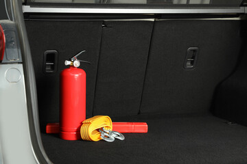 Red fire extinguisher, towing strap and foldable emergency warning triangle in trunk, space for text. Car safety