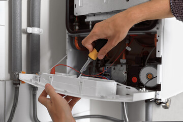 Man repairing gas boiler with screwdriver indoors, closeup
