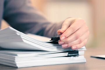 Woman attaching documents with metal binder clip at table in office, closeup
