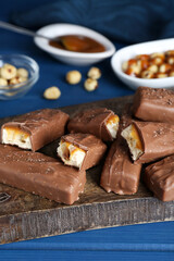 Tasty chocolate bars with caramel and nuts on light blue wooden table