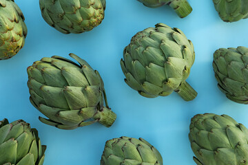 Obraz premium Whole fresh raw artichokes on light blue background, flat lay