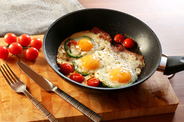 Delicious fried eggs with bacon, tomatoes and pepper served on wooden table