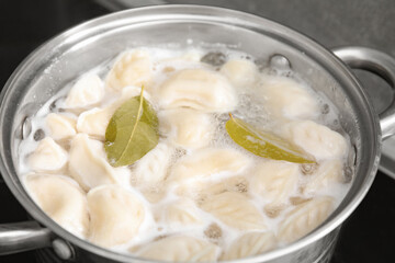 Cooking dumplings (varenyky) with tasty filling and bay leaves in pot indoors, closeup