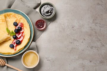 Delicious crepes with jam, honey and blueberries on light grey table, flat lay. Space for text