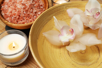 Bowl with water, flowers, sea salt and burning candles on bamboo mat, closeup. Spa treatment