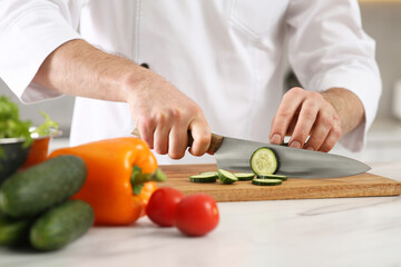 Chef cutting cucumber at marble table in kitchen, closeup
