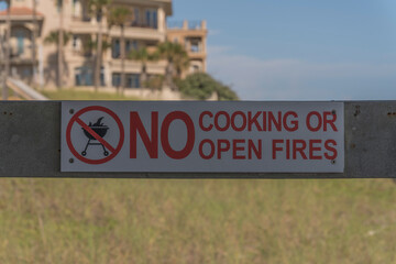Obraz premium Signage on a wood railing with No Cooking or Open Fire at Destin, Florida outdoors. Close-up of a sign against the grasses and buildings at the blurred background.