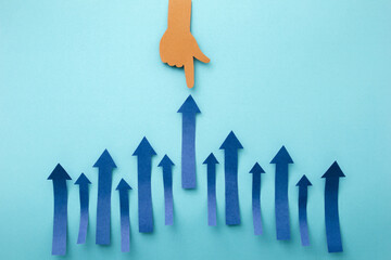 Hand pointing up arrow made of cut paper on blue background. Business and success concept.