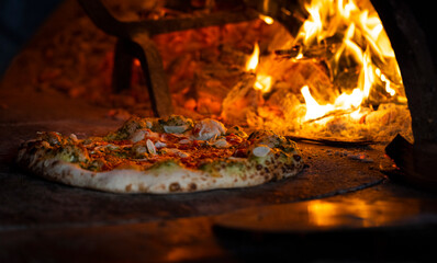 Pizza in the traditional pizza oven with a wood fire. Close up of hot cooking.