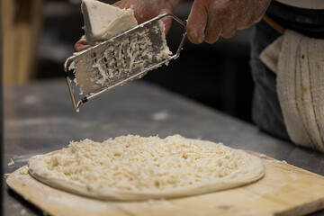 Close up of the making process, male hands rubbed cheese grated. Prepared uncooked raw making pizza...