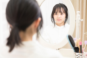 ドレッサーの鏡で顔を見ている若い女性