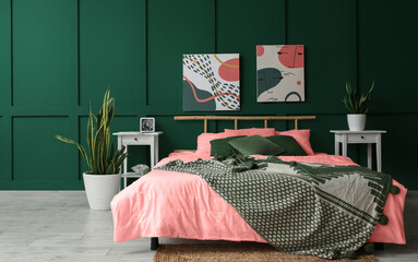 Interior of stylish bedroom with big bed, paintings and houseplants near green wall