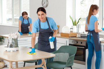 Female janitor cleaning dining table in kitchen