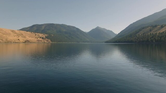 Aerial moving horizontally over scenic alpine lake with mountains behind