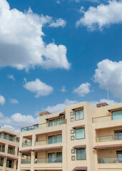 Vertical White puffy clouds Low rise residential buildings at La Jolla in California. Buildings exterior with glass railings and canopies on the windows and terrace against the sky background.