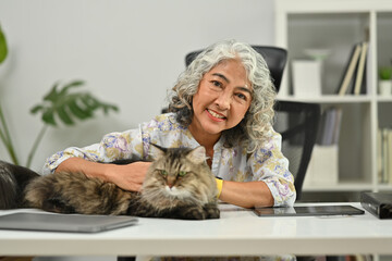 Carefree middle aged woman petting her lovely fluffy cat and smiling to camera. Love, domestic pet concept